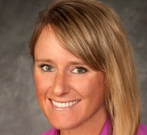 Woman with dark blonde hair wearing a pink collared shirt.