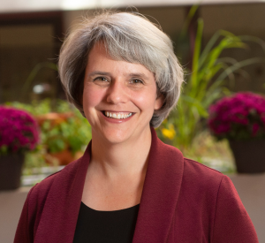 Woman with short gray hair wearing a dark red sweater over a black shirt.