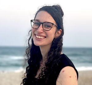 Woman with dark curly hair wearing dark glasses and a black sleeveless shirt.