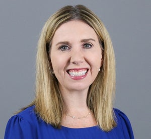 Woman with blonde hair wearing a dark blue blouse and a silver necklace.