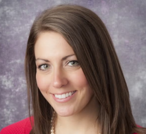 A woman with brown hair wearing a red cardigan and a pearl necklace.