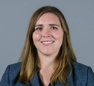 Woman with long brown hair and highlights wearing a navy blue blazer.