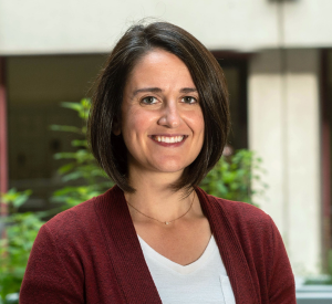 Woman with dark brown short hair wearing a dark red cardigan over a white shirt.