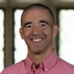 Man with very short dark hair wearing a pink collared shirt.