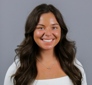 Woman with long brown hair wearing a white shirt and a silver necklace.