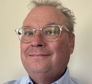 Man with short gray hair wearing silver glasses and a light blue collared shirt.