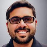 Man with dark hair and a beard wearing glasses and a dark gray collared shirt.