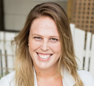 A woman with dark blonde hair wearing a white collared shirt.