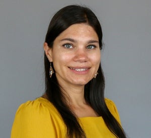 Woman with long brown hair wearing a yellow blouse and gold earrings.