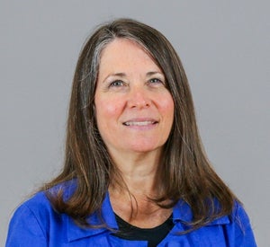 Woman with dark brown and gray hair wearing a bright blue blouse over a black top.