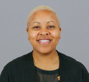 Woman with short blonde hair wearing a black sweater over a black top and a gold necklace.