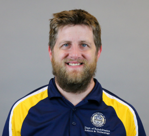 Man with light brown hair and a beard wearing a Pitt polo with dark blue, yellow and white colors.