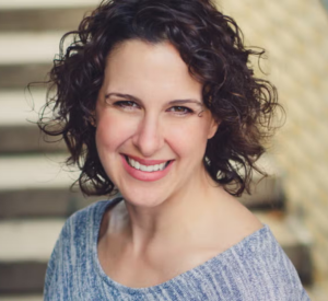 Woman with short brown curly hair wearing a gray shirt.