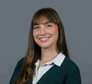 Woman with long brown hair wearing a black cardigan over a white collared shirt.