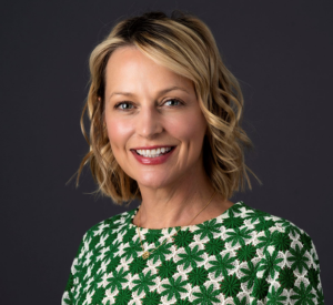 Woman with short blonde hair that is curled wearing a green and white crochet shirt.