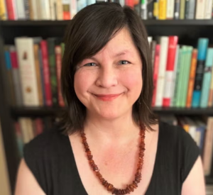 Woman with short black hair wearing a black blouse with a brown beaded necklace.