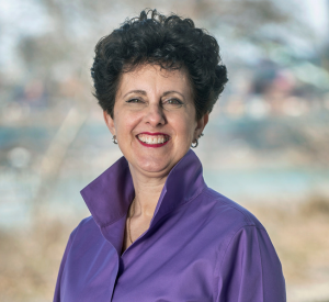 Woman with short, curly black hair wearing a purple blouse.