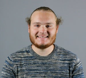 Man with red hair and a beard wearing a blue and tan striped sweater.