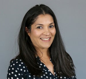 Woman with long black hair wearing a black blouse with white polka dots.