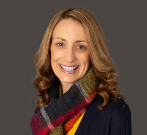 Woman with dark blonde hair wearing a black shirt with a black, red, and yellow scarf.