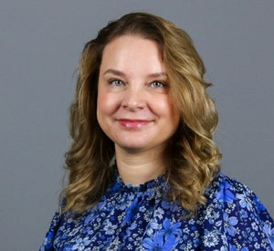 Woman with light brown curly hair wearing a blue floral print shirt.