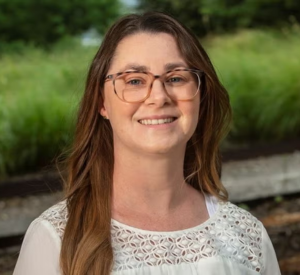 Woman with brown hair wearing a white shirt and brown glasses.