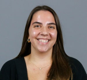 Woman with long brown hair wearing a black sweater, gold earrings and a gold necklace.