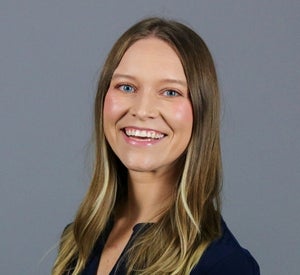 Woman with long brown hair with blonde highlights wearing a black blouse.