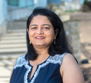 Woman with black hair wearing a navy blue short sleeve top with white patterns on the shoulder.