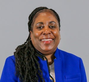 Woman with long dark hair pulled back into a ponytail, draped over her shoulder, wearing a royal blue blazer.