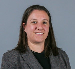 Woman with short brown hair wearing a gray blazer over a black blouse.