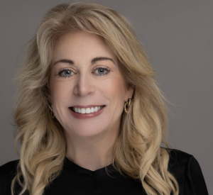 Woman with long blonde hair wearing a black shirt and gold earrings.