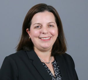 Woman with short brown hair wearing a black blazer over a black and white patterned top and a silver necklace.