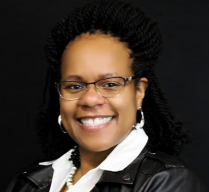 Woman with dark hair wearing a black leather jacket over a white collared shirt with pearl earrings and a necklace.