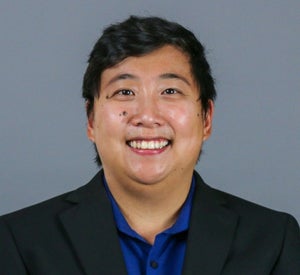 Woman with short black hair wearing a black blazer over a dark blue collared shirt.