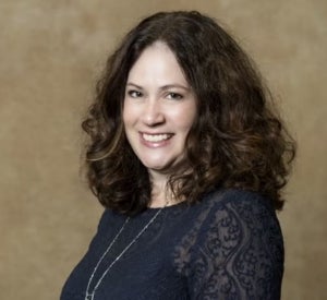 Woman with dark brown, curly, shoulder-length hair in a black blouse.