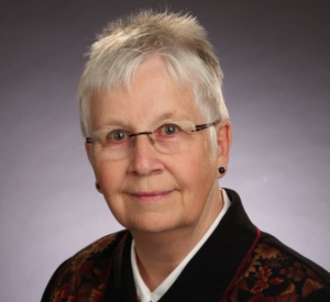 Woman with white hair wearing a black and brown velvet shirt over a white collared shirt.