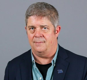 Man with short grey hair wearing a dark blue suit, plaid green shirt and a Pitt enamel pin.