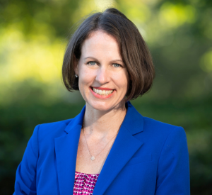 Woman with short brown hair wearing a bright blue blazer over a pink and white patterned top.