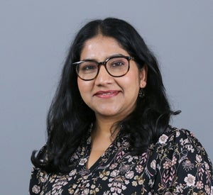 Woman with medium length, black hair wearing bold glasses and a floral top.