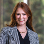 Woman with red hair wearing a black and white checkered blazer over a black blouse and a gold necklace.