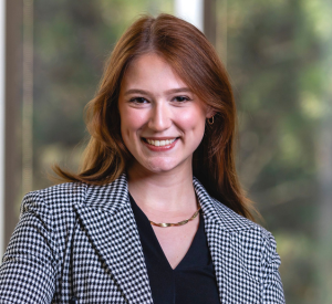 Woman with red hair wearing a black and white checkered blazer over a black blouse and a gold necklace.