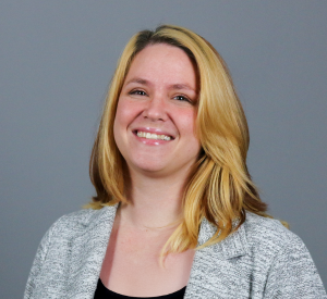 A woman with brown and bright blonde hair wearing a gray blazer over a black shirt.