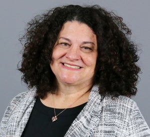 Woman with medium, curly dark brown hair wearing a white striped blazer.