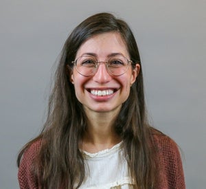 Woman with long brown hair wearing a burnt orange sweater.