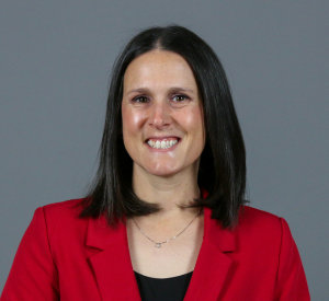 Woman with short black hair wearing a red blazer over a black top with a gold necklace.