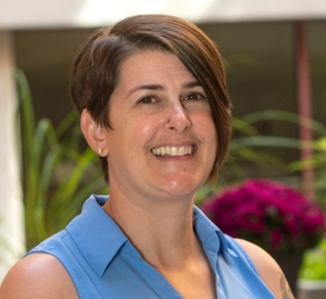 Woman with short brown hair wearing a sleeveless, collared light blue top,