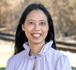 Woman with long black hair wearing a light purple collared blouse.