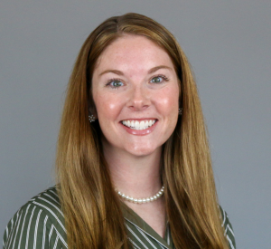 Woman with dark blonde hair wearing a green and white striped blouse with a pearl necklace.