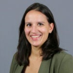 Woman with medium length, dark brown hair, wearing an army green blazer.